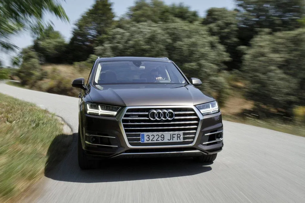 2027 Audi Q7 Luxus-SUV mit drei Sitzreihen fährt mit eingeschalteten LED-Scheinwerfern auf einer befestigten Straße