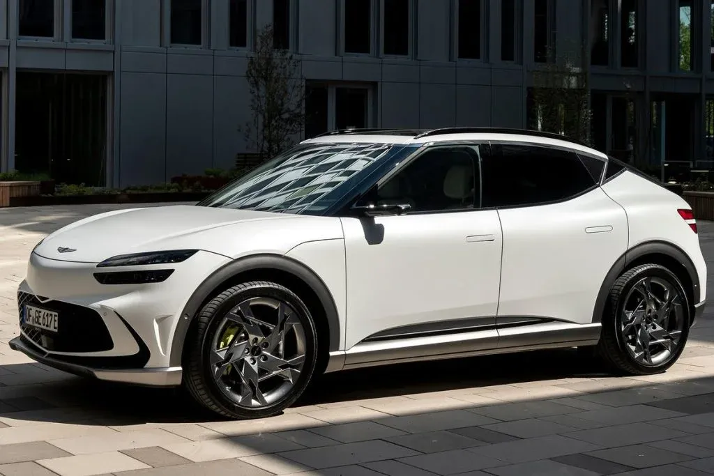 2027 Genesis GV60 Magma elektrischer Performance-Crossover in leuchtendem Orange, aus der vorderen Dreiviertelansicht auf einer Straße gezeigt