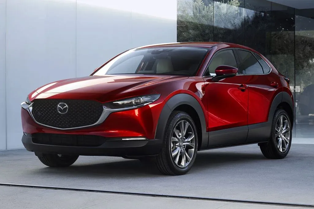 Mazda3 Schrägheck und Mazda CX-30 Crossover bei Sonnenuntergang auf einer modernen Straße geparkt