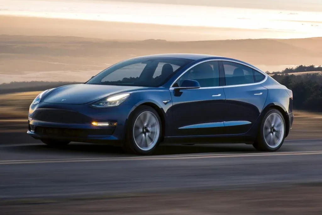 Tesla Model 3 fährt bei Tageslicht durch eine vorstädtische Wohnstraße nahe Häusern
