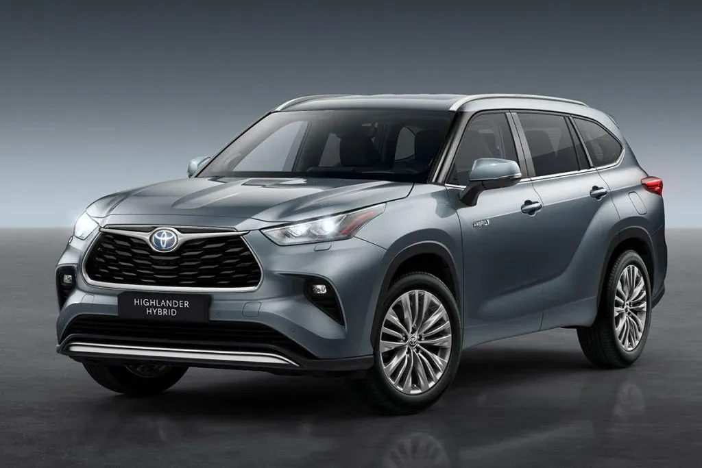 Toyota-Highlander-artiger dreireihiger SUV fährt auf einer Vorstadtstraße mit einer Ladestation für Elektrofahrzeuge im Hintergrund